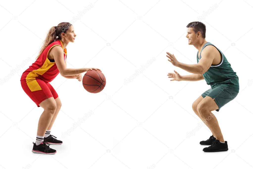 Young woman playing basketball against a young man