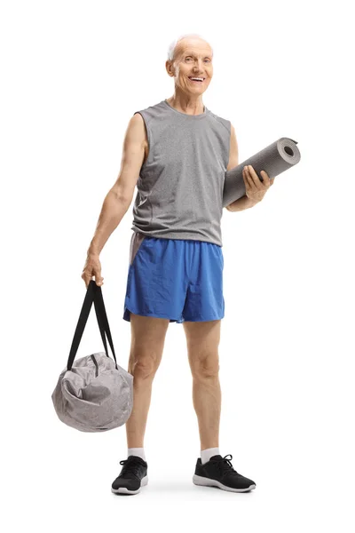 Hombre mayor de pie y sosteniendo una bolsa de deporte y una alfombra de ejercicio — Foto de Stock