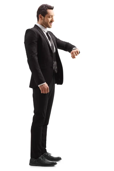 白い背景に隔離された腕時計を見てスーツを着たビジネスマンのフルレングスプロフィールショット — ストック写真