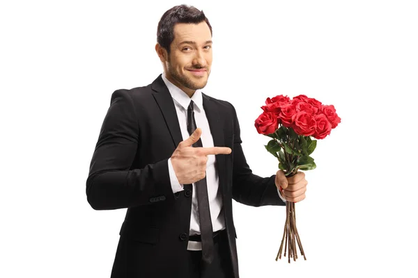 Jovem bonito atrevido segurando um monte de rosas vermelhas e apontar — Fotografia de Stock
