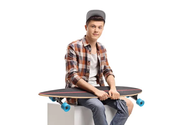 Männlicher Teenager sitzt mit einem Longboard — Stockfoto