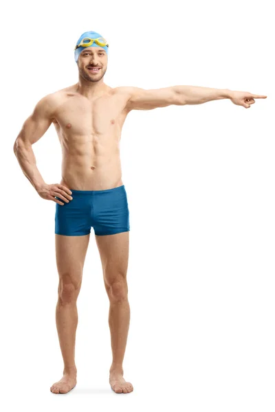 Young man in swimming shorts, googles and a cap pointing to the — Stock Photo, Image