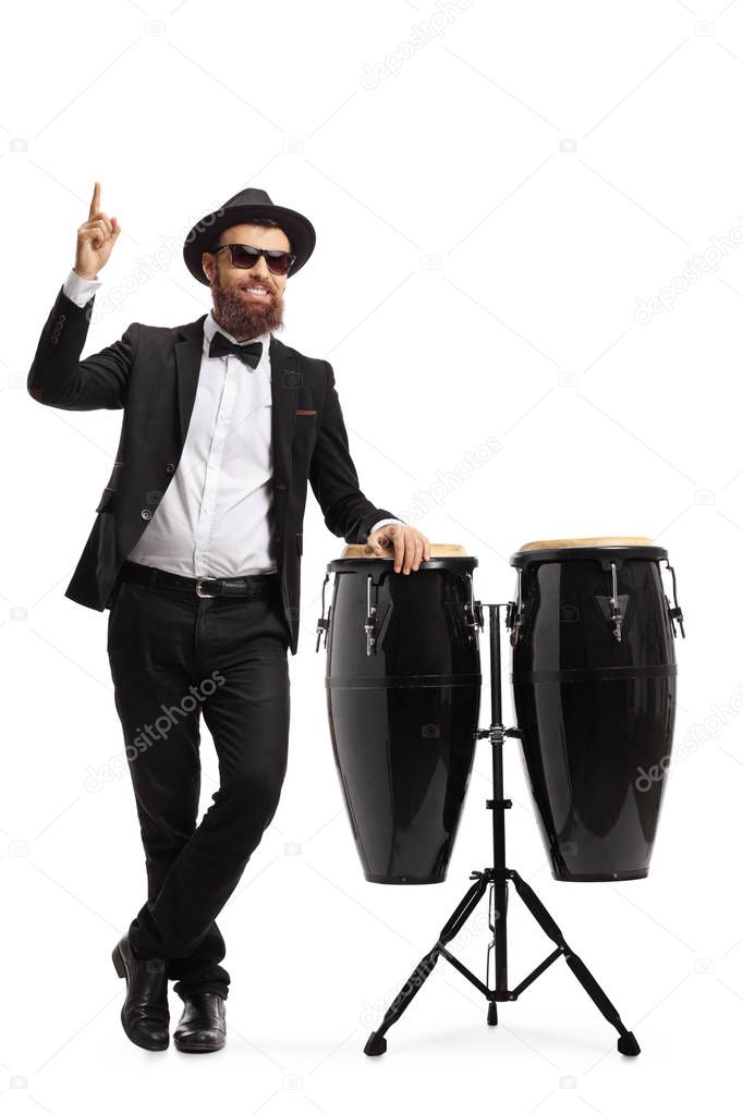 Male musician in a suit posing next to conga drums and pointing 