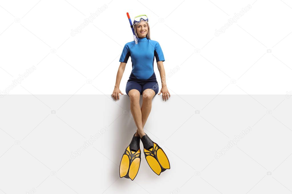 Full length portrait of a young woman with a diving equipment sitting on a panel isolated on white background