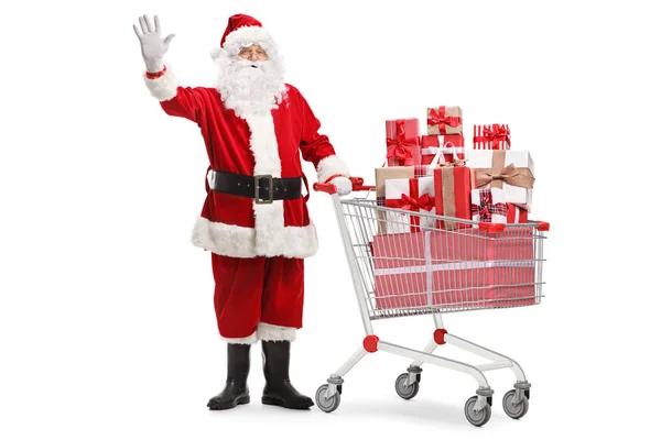 Papai Noel de pé com um carrinho de compras cheio de presentes e w — Fotografia de Stock