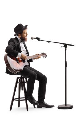 Adam mikrofonda şarkı söylüyor ve akustik gitar çalıyor. 