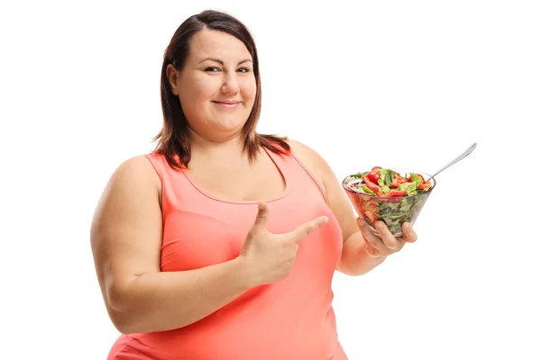 Mulher alegre gordinha segurando uma tigela de salada fresca e apontando — Fotografia de Stock