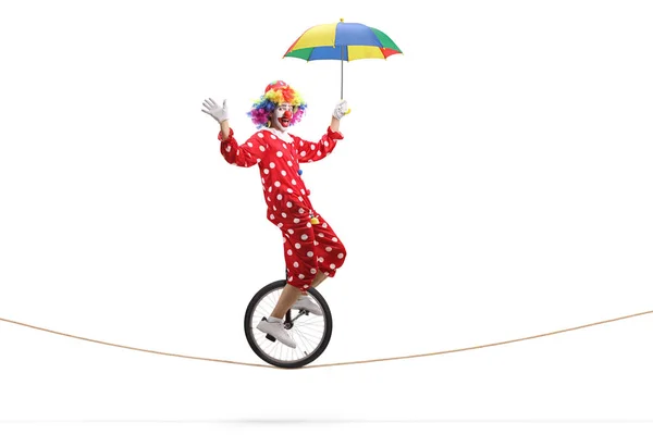 Clown riding a unicycle on a rope and holding an umbrella — Stock Photo, Image