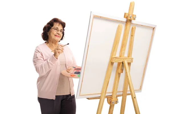 Mulher idosa feliz com um pincel e pinturas pintura em uma tela — Fotografia de Stock