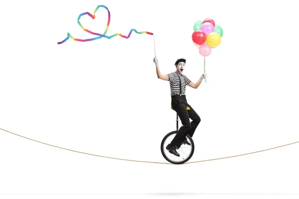 Mime riding a unicycle on a rope holding a ribbon with a heart s — Stock Photo, Image