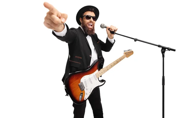 Hombre con una guitarra eléctrica cantando en un micrófono y señalando — Foto de Stock