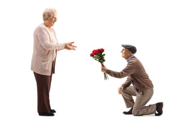 Kıdemli adam diz çökmüş ve bir üst düzey kırmızı gül bir demet veren 