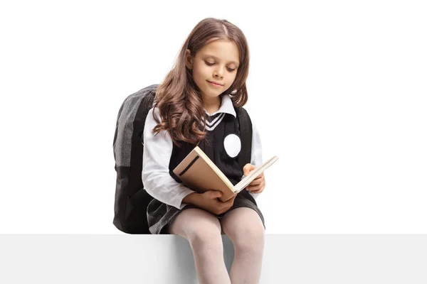 Schoolgirl ina üniforma bir panelde oturan ve bir kitap okuma — Stok fotoğraf
