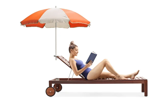 Giovane donna che legge un libro e si rilassa su un lettino sotto l'ombrello — Foto Stock