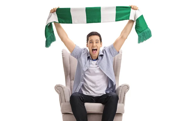 Excited man sitting in an armchair and cheering with a scarf — Stock Photo, Image