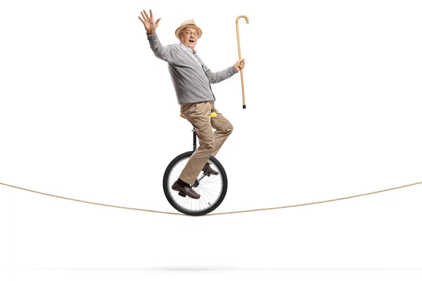 Homme âgé chevauchant un monocycle sur une corde et tenant une marche — Photo