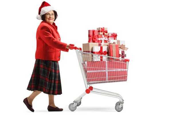 Anciana con un sombrero de navidad empujando un carrito de compras con — Foto de Stock