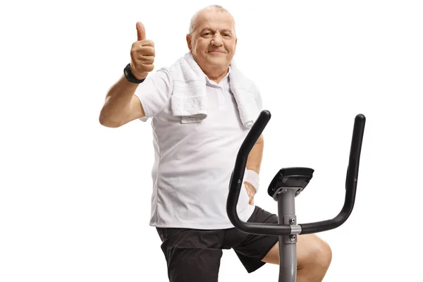 Mogen man på en motionscykel som visar tummen upp — Stockfoto