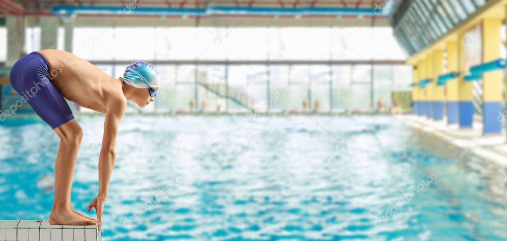 Boy swimmer on the start position at a swimming pooln 