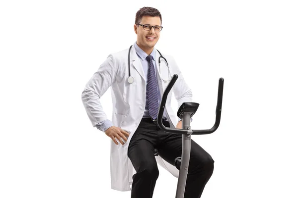 Young male doctor on a stationary bike looking at the camera and — Stock Photo, Image
