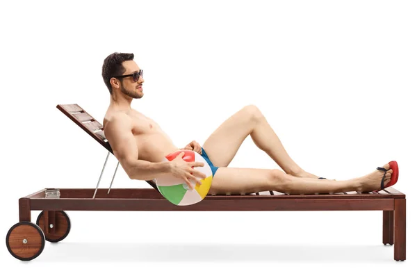 Young fit man on a sunbed holding an inflatable ball — Stock Photo, Image