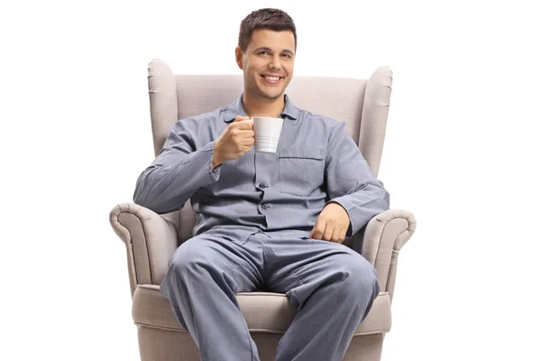 Fröhlicher junger Mann mit einer Tasse im Sessel — Stockfoto