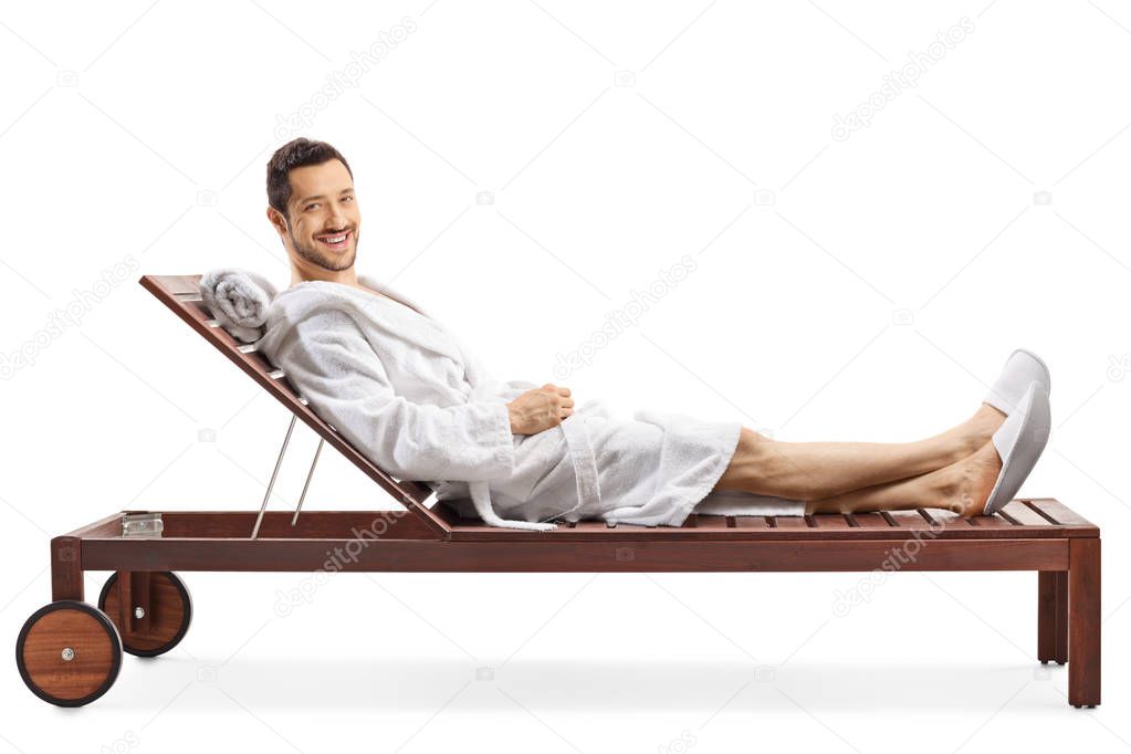 Cheerful young man in a bathrobe relaxing on a lounge chair and 