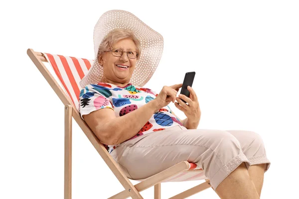 Elderly woman on a vacation with a phone sitting in a deck chair — Stock Photo, Image