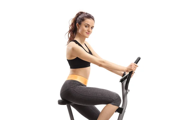 Jovem mulher em forma montando uma bicicleta de exercício e olhando para a câmara — Fotografia de Stock