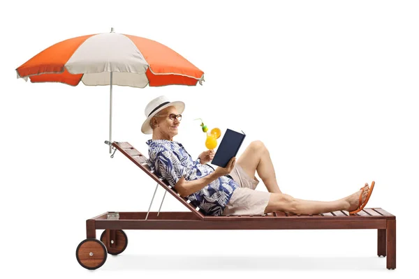 Hombre mayor disfrutando en una tumbona con un libro y un cóctel — Foto de Stock