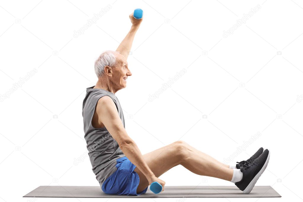 Elderly man sitting on a mat and exercising with dumbbells 