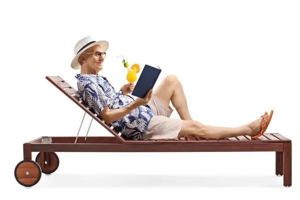 Anciano turista masculino en una cama de salón leyendo un libro y sosteniendo —  Fotos de Stock