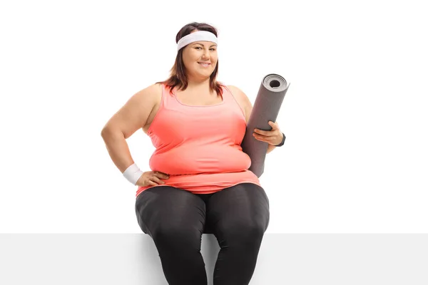Plus Size jong vrouw met een oefening mat zittend op een panel — Stockfoto