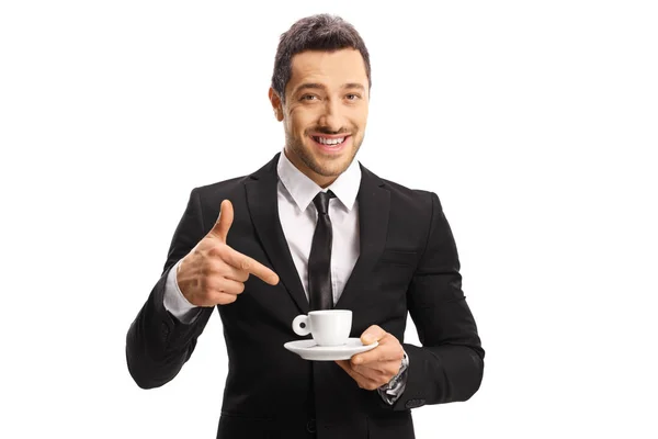 Jeune homme joyeux dans un costume tenant une tasse de café et pointin — Photo