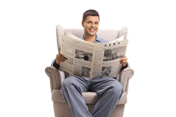 パジャマ姿の若者が新聞と一緒に肘掛け椅子に座った — ストック写真