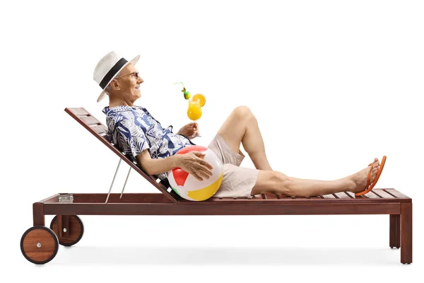 Elderly man lying on a sunbed drinking a cocktail and holding an — Stock Photo, Image