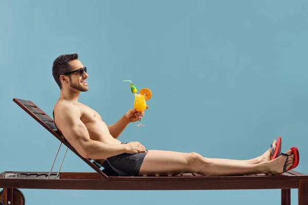 Fit man enjoying a cocktail on a sunbed — Stock Photo, Image