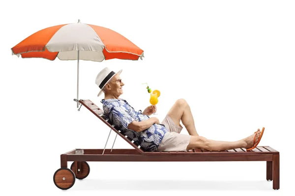 Старший чоловік розслабляється на пляжному ліжку під парасолькою з півень — стокове фото