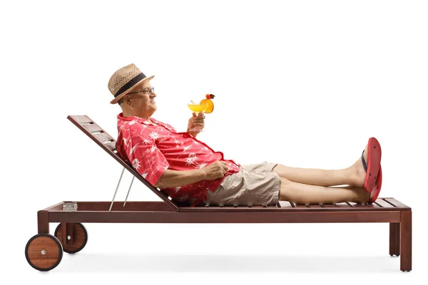 Mature man holding a cocktail and relaxing on beach bed — Stock Photo, Image