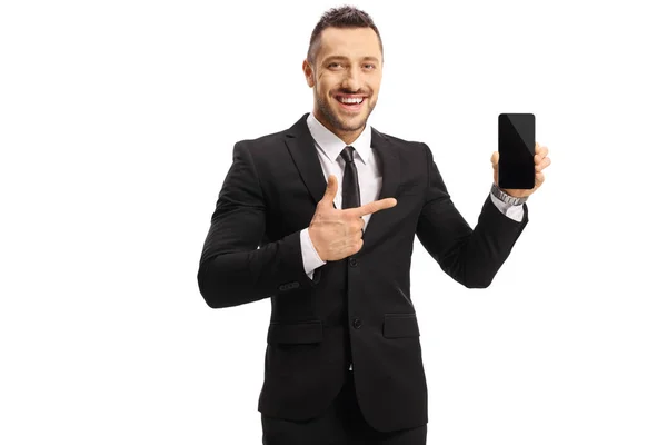 Cheerful young man in a suit holding a mobile phone and pointing — Stock Photo, Image