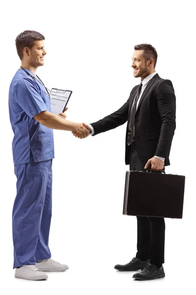 Jovem médico masculino em um uniforme azul apertando as mãos com um busines — Fotografia de Stock