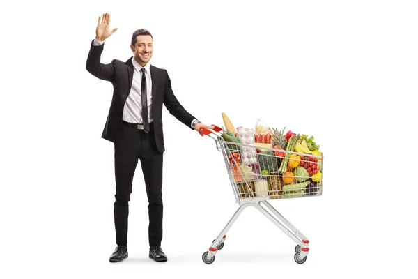 Affärsman med en kundvagn full av livsmedelsprodukter viftar på — Stockfoto