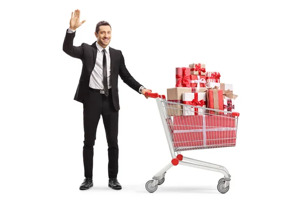 Businessman with a shopping cart full of presents waving — Stock Photo, Image