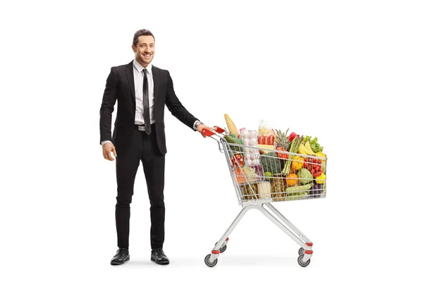 Empresario posando con un carrito de compras con comida — Foto de Stock