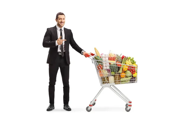 Ung man i en kostym stående med en kundvagn full av mat en — Stockfoto