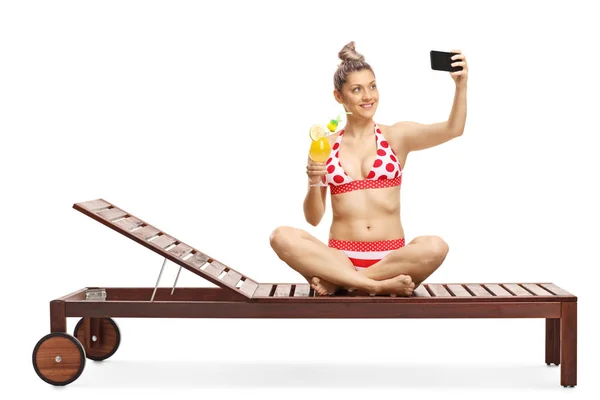 Young female in bikini drinking a cocktail and taking a selfie w — Stock Photo, Image