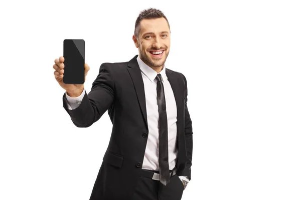 Молодой человек в костюме показывает мобильный телефон и улыбается — стоковое фото