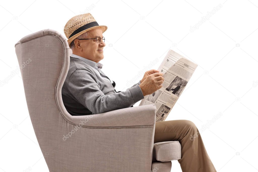 Cheerful mature man sitting in an armchair and reading a newspap