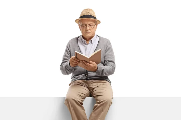 Starszy pan siedzi na panelu czytając książkę — Zdjęcie stockowe