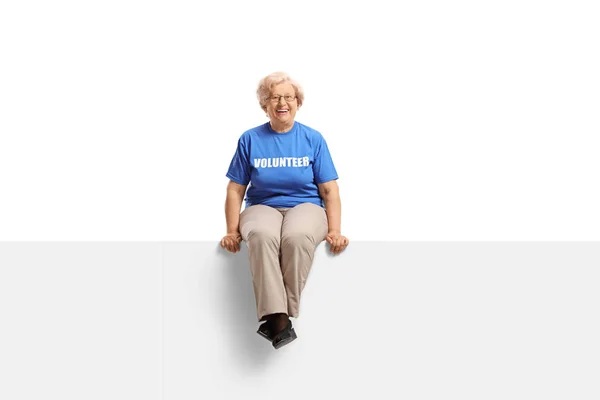 Vrolijke Senior Lady vrijwilliger zittend op lege witte banner — Stockfoto